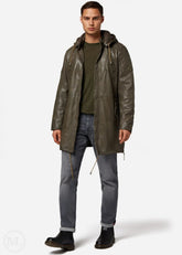 Man wearing a olive green leather coat, green shirt, and gray jeans on a white background