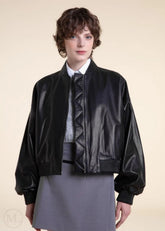 woman wearing a black leather bomber jacket on a beige background